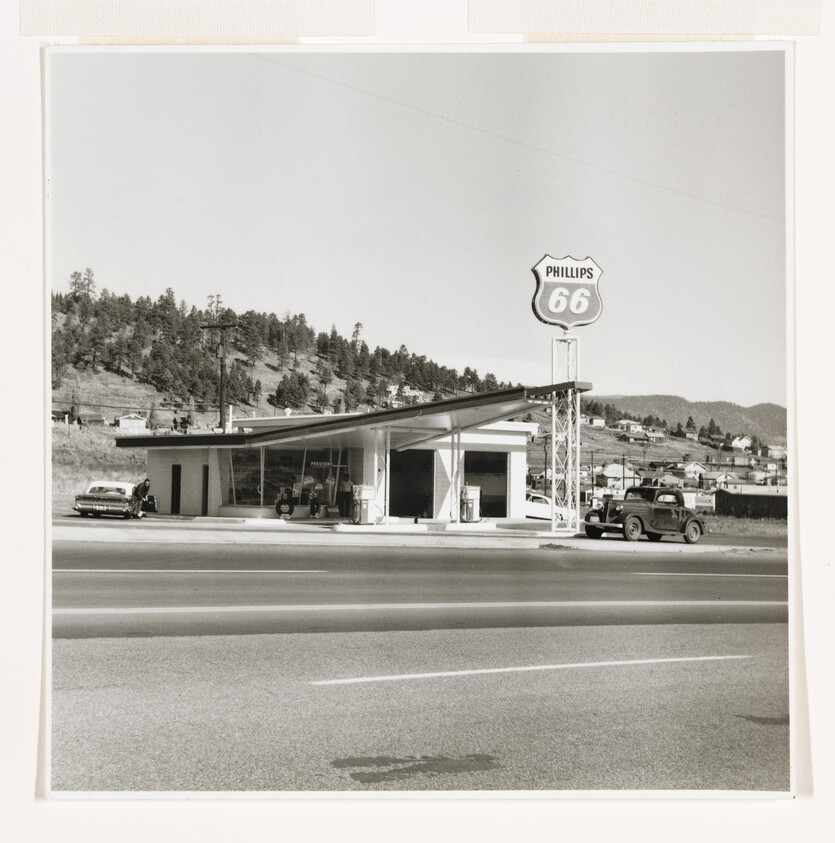 Vintage Phillips 66 gas station with cars parked beside pumps along a highway.