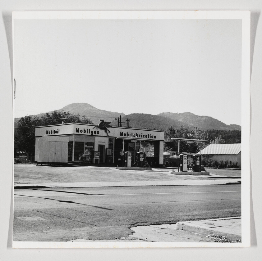 A Mobilgas station with several vintage pumps sits by a road with mountains behind it.