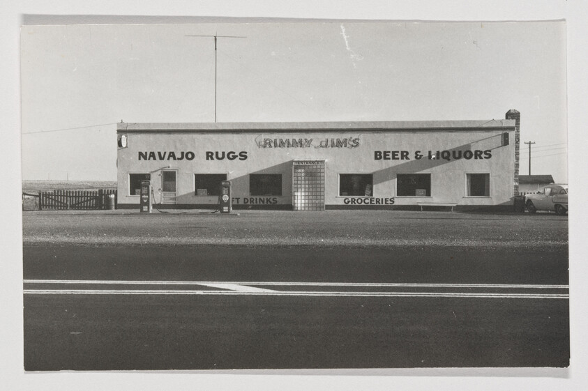 Small roadside store with signs for Navajo Rugs and Beer & Liquors and two gas pumps.