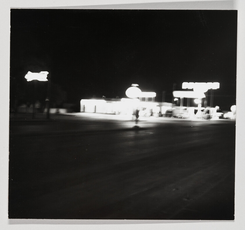 Brightly lit gas station and pumps blurred across an empty dark street at night.