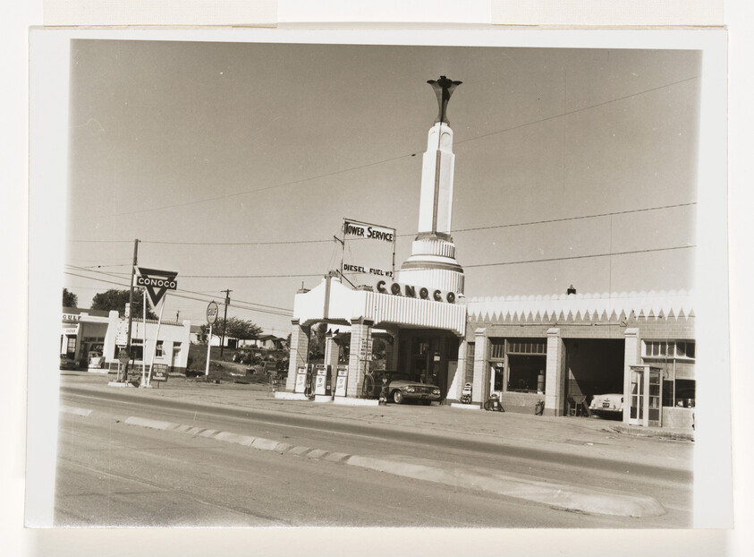 Vintage Conoco service station with tall tower and cars refueling at the pumps.