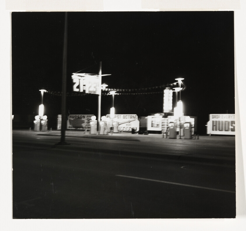 A brightly lit gas station with several fuel pumps and signs glowing at night.