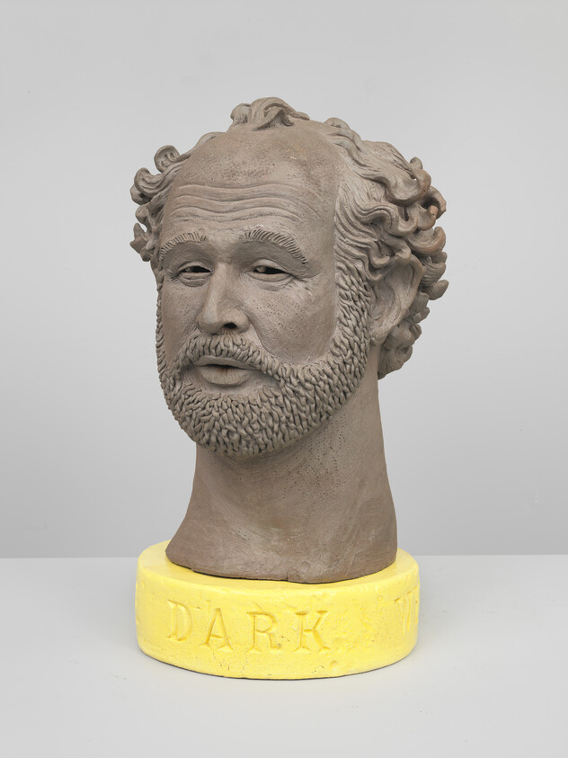 Sculpted male bust with curly hair and beard mounted on a yellow base.