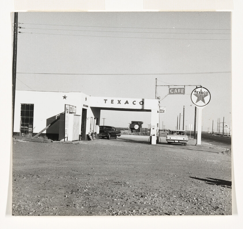A Texaco gas station and canopy with two cars parked near pumps and a cafe sign.