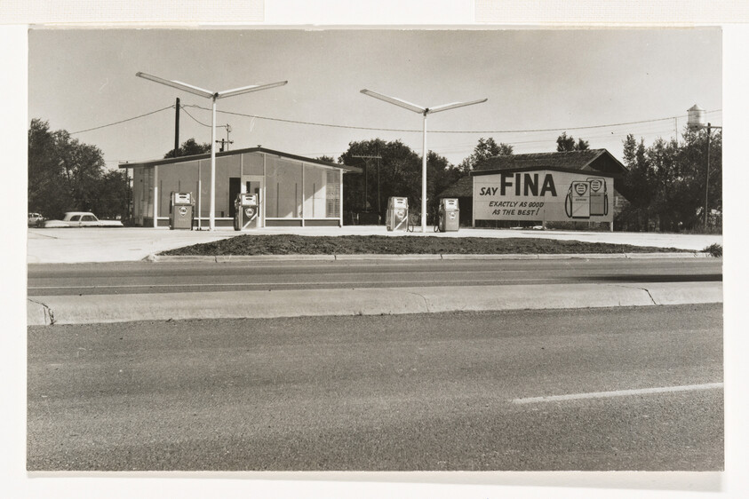 A vintage FINA gas station with pumps and a large "SAY FINA" advertisement beside the building.