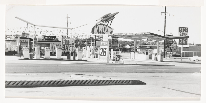 Vintage gas station with a large rooftop sign and price signs showing 26 and 29 cents per gallon.