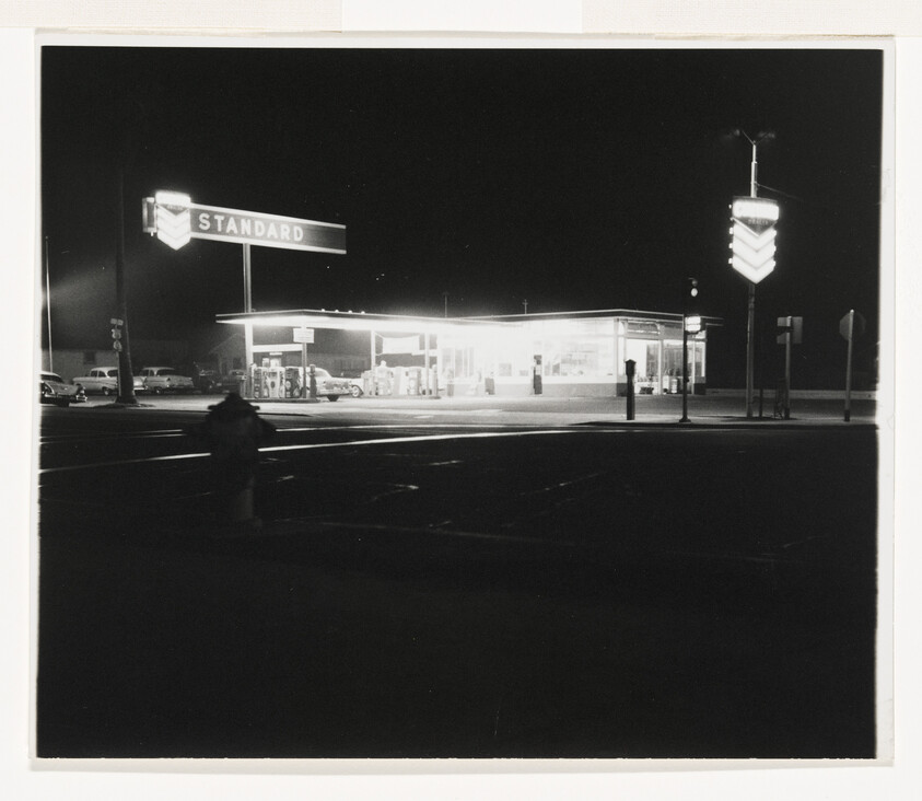 A brightly lit Standard gas station glows at night beneath a large neon sign.
