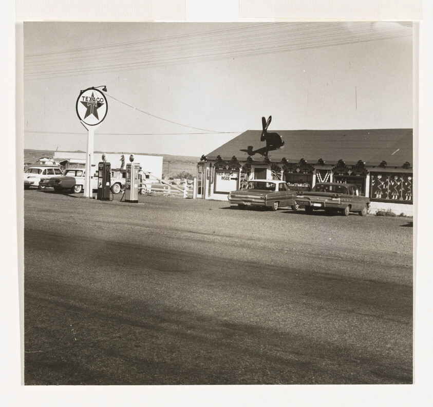 Texaco gas station with two vintage cars parked beside pumps and a rabbit sign on roof.