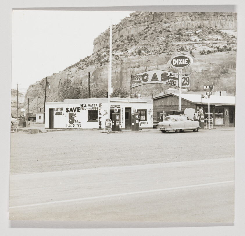 A vintage Dixie gas station with pump attendant servicing a car in front of a rocky cliff.