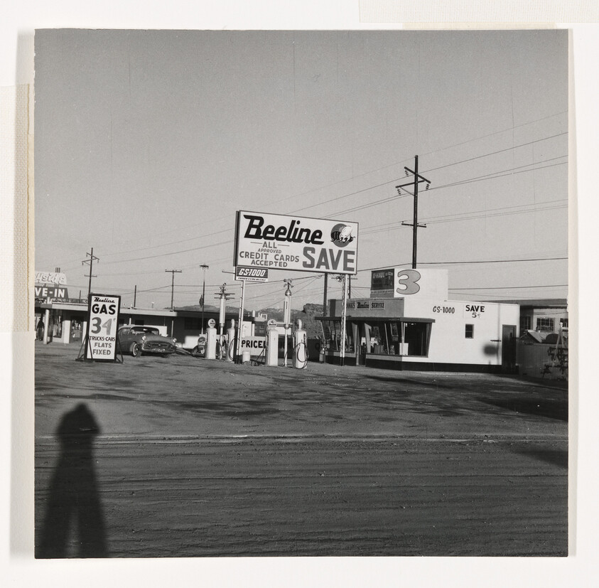 A vintage Beeline gas station with multiple pumps and a large roadside sign advertising low prices.