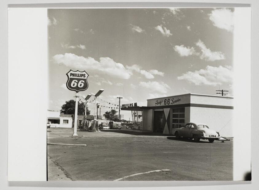 Vintage Phillips 66 gas station with pumps and a parked 1950s car under a cloudy sky.