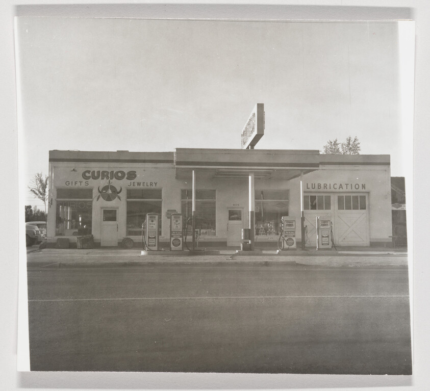 Vintage gas station with four fuel pumps, a curios gift shop on left and lubrication garage on right.