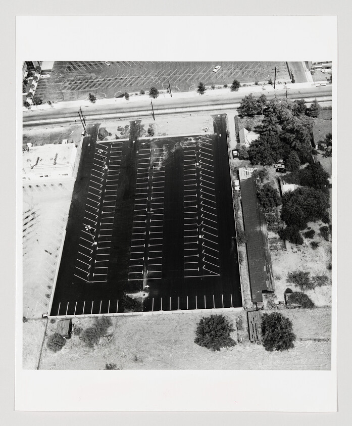 Aerial view of a large empty parking lot with white painted parking lines and nearby trees.