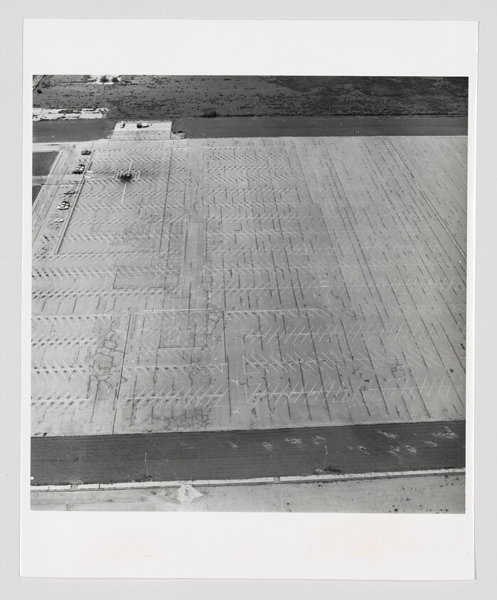 A large empty cracked parking lot with painted parking lines and a few cars in the corner.