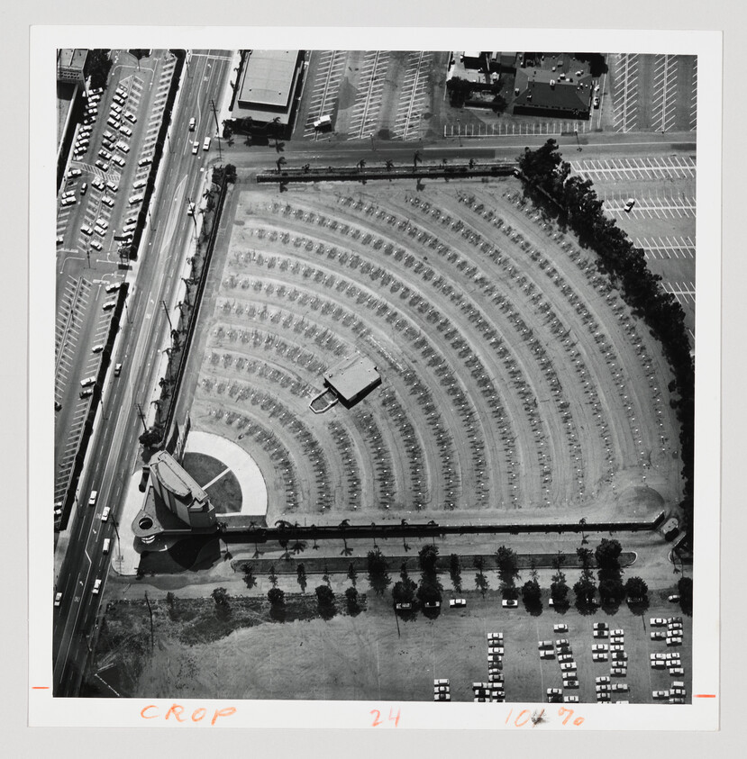 Aerial view of a large semicircular drive-in theater with rows of parked cars and projection tower.