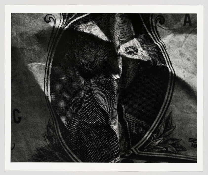 A creased one-dollar bill portrait with dark shadows and a vertical fold down the center.
