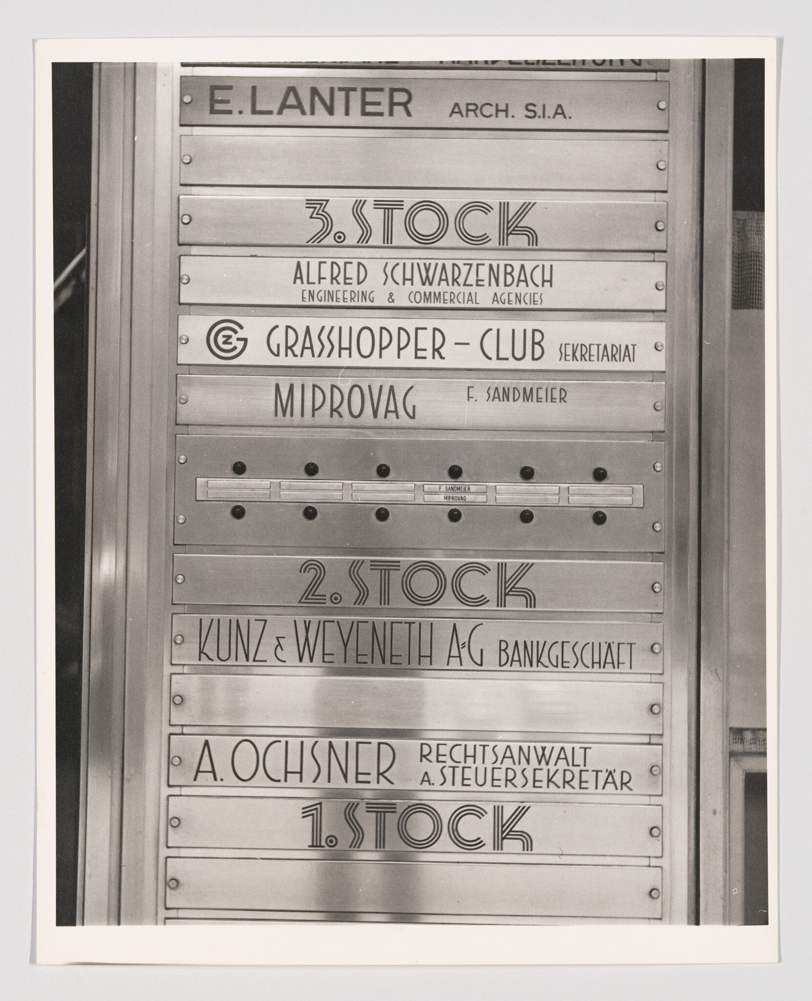 Metal building directory panel showing company names, floor numbers, and intercom buttons.