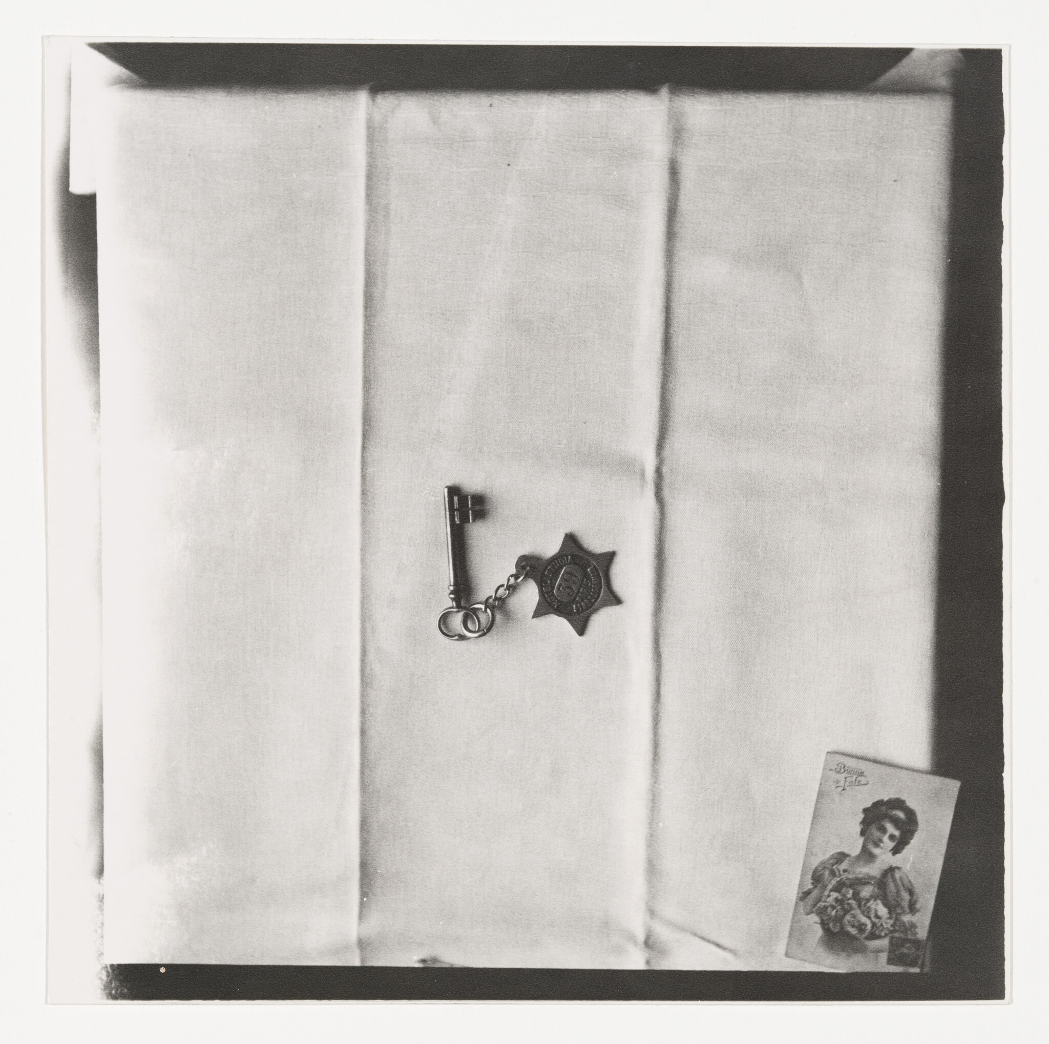 A small antique key with a star-shaped badge lies on folded white cloth beside a vintage portrait card.
