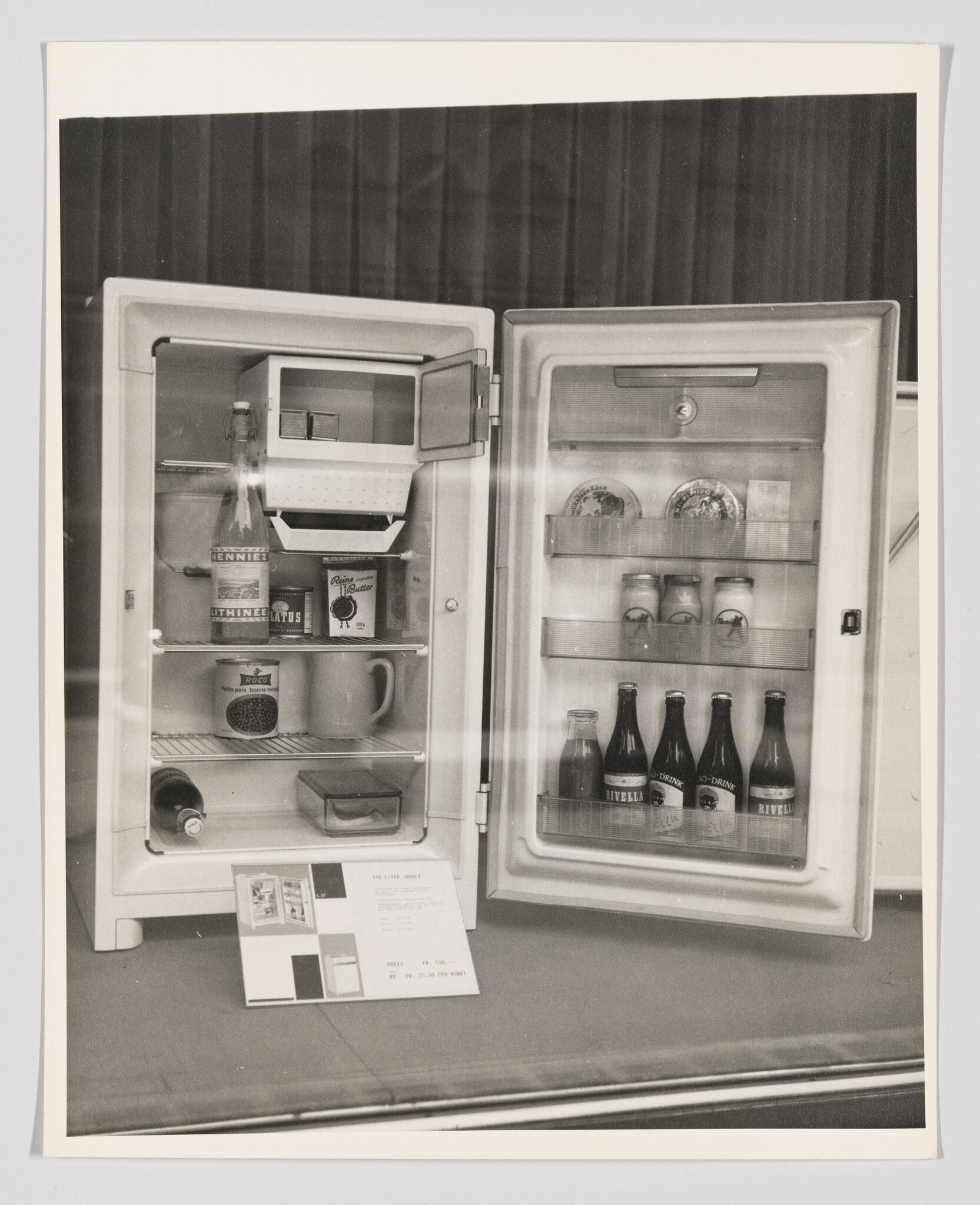 Small vintage refrigerator with both doors open showing bottles, jars, and a product information card.