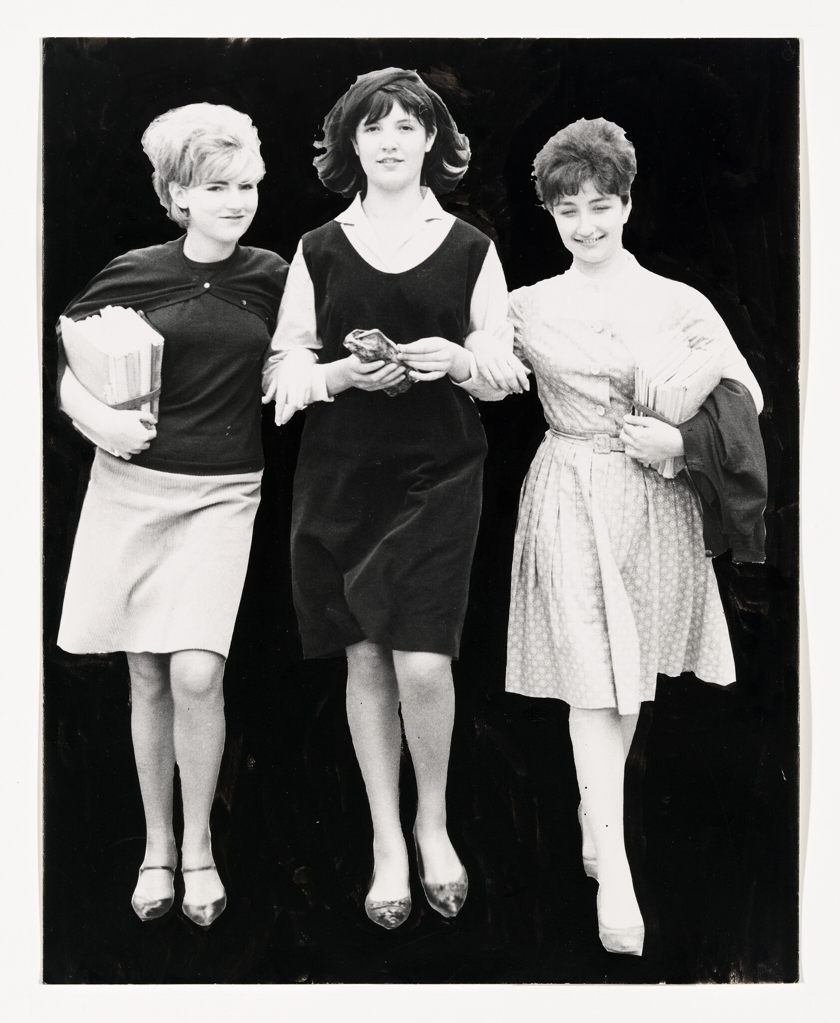 Three young women walk arm in arm down a street carrying books and smiling.