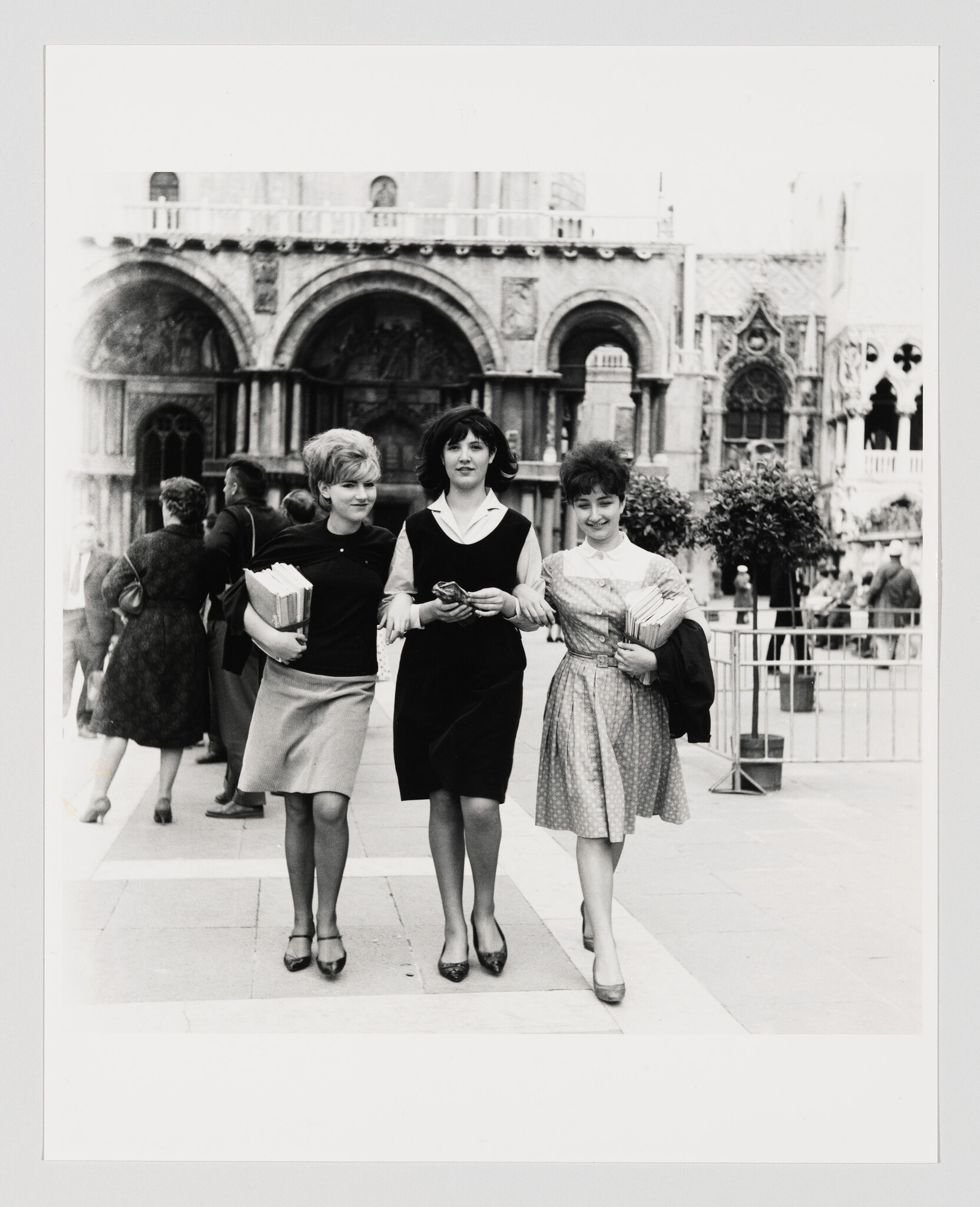 A group of three young white women have their arms connected as they walk forward