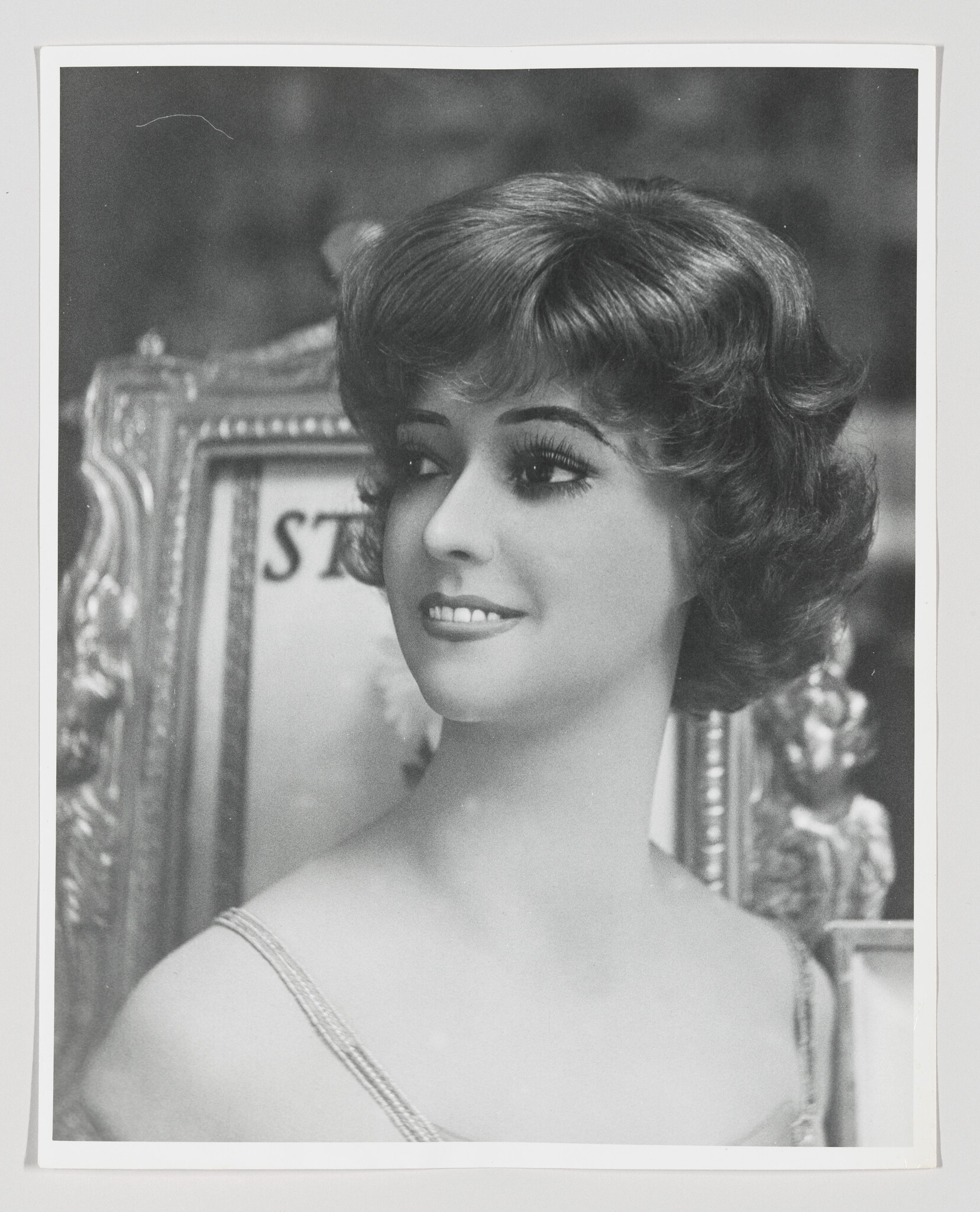 Young woman with short curled hair smiles and looks to the right in a framed portrait setting.