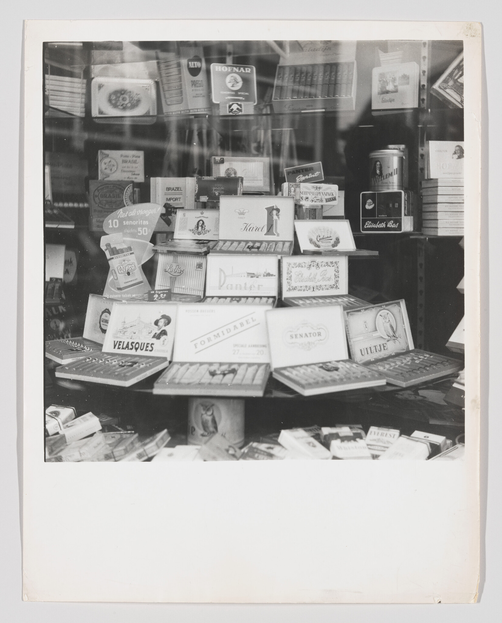 Multiple cigar and cigarette boxes neatly arranged in a shop window display behind glass.