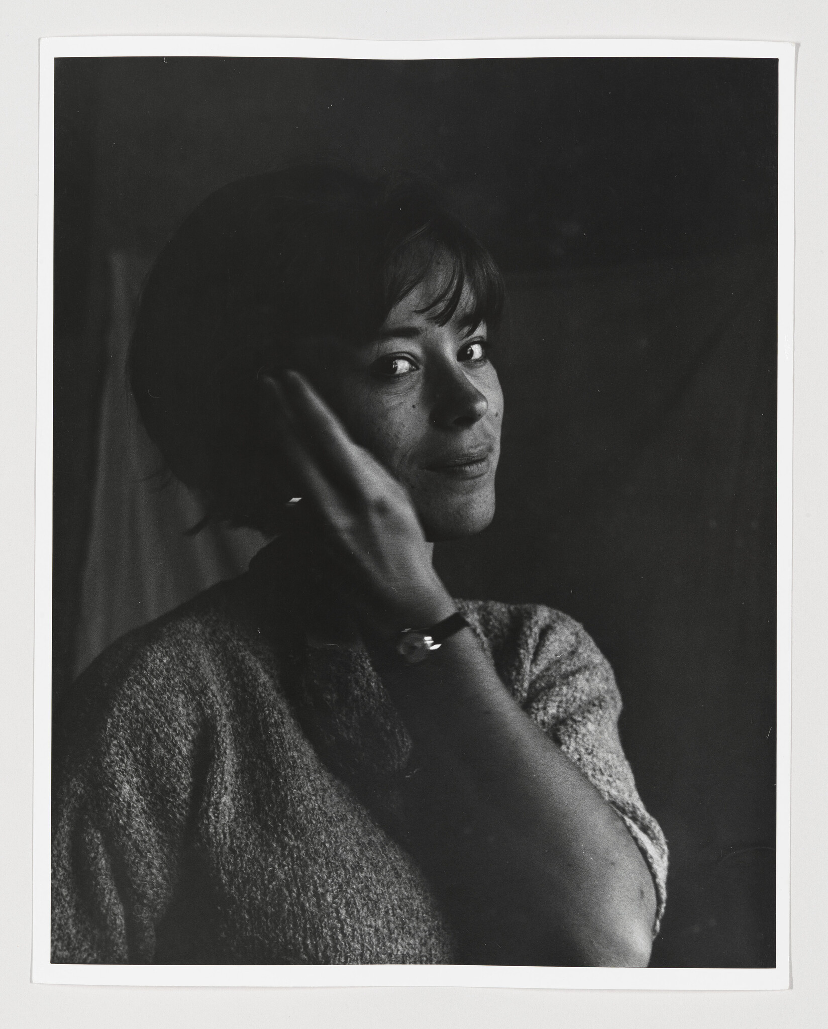 A woman looks over her shoulder while lifting her hand to tuck hair behind her ear.