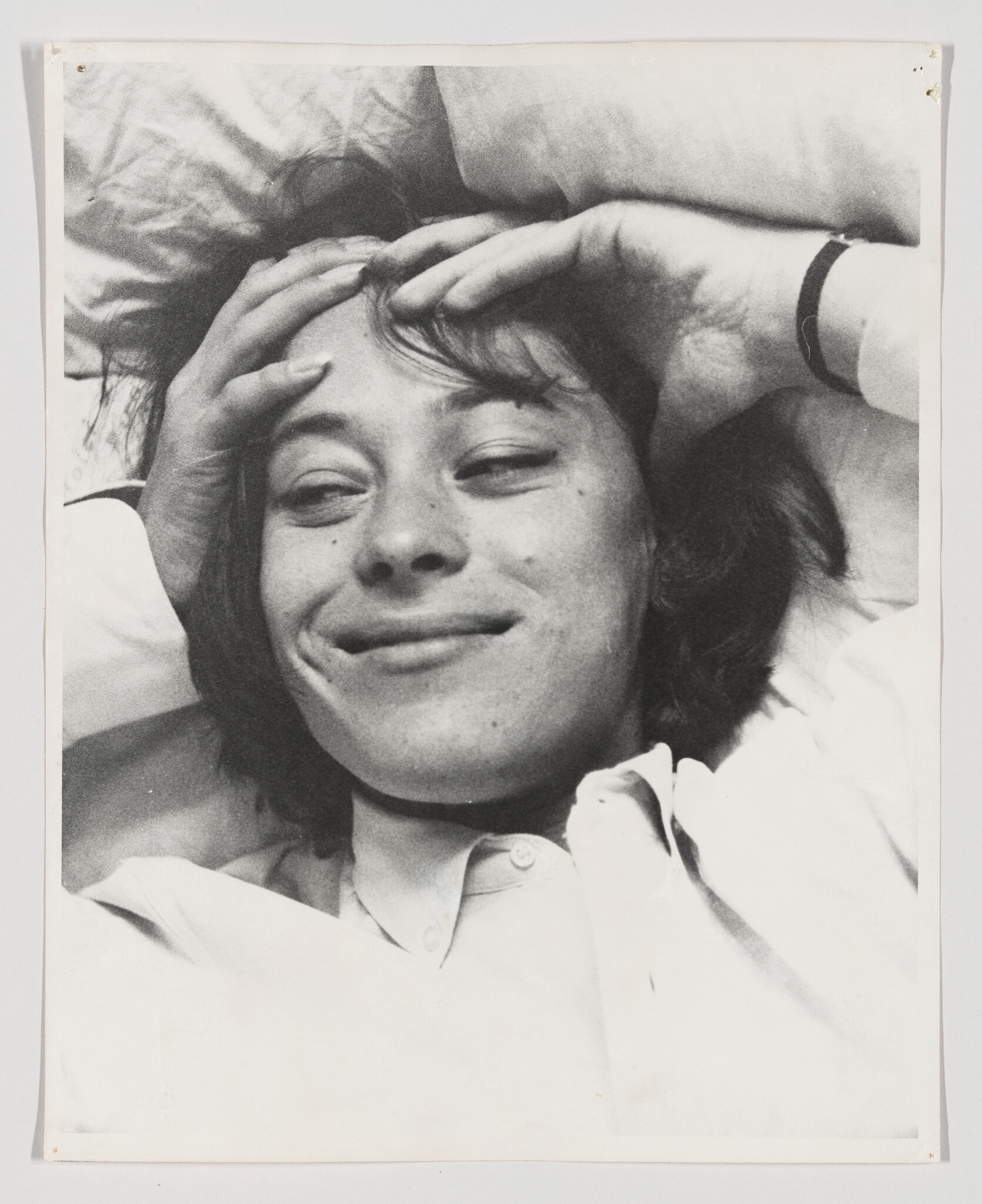 Young person lying on a pillow smiling with hands resting on their head.