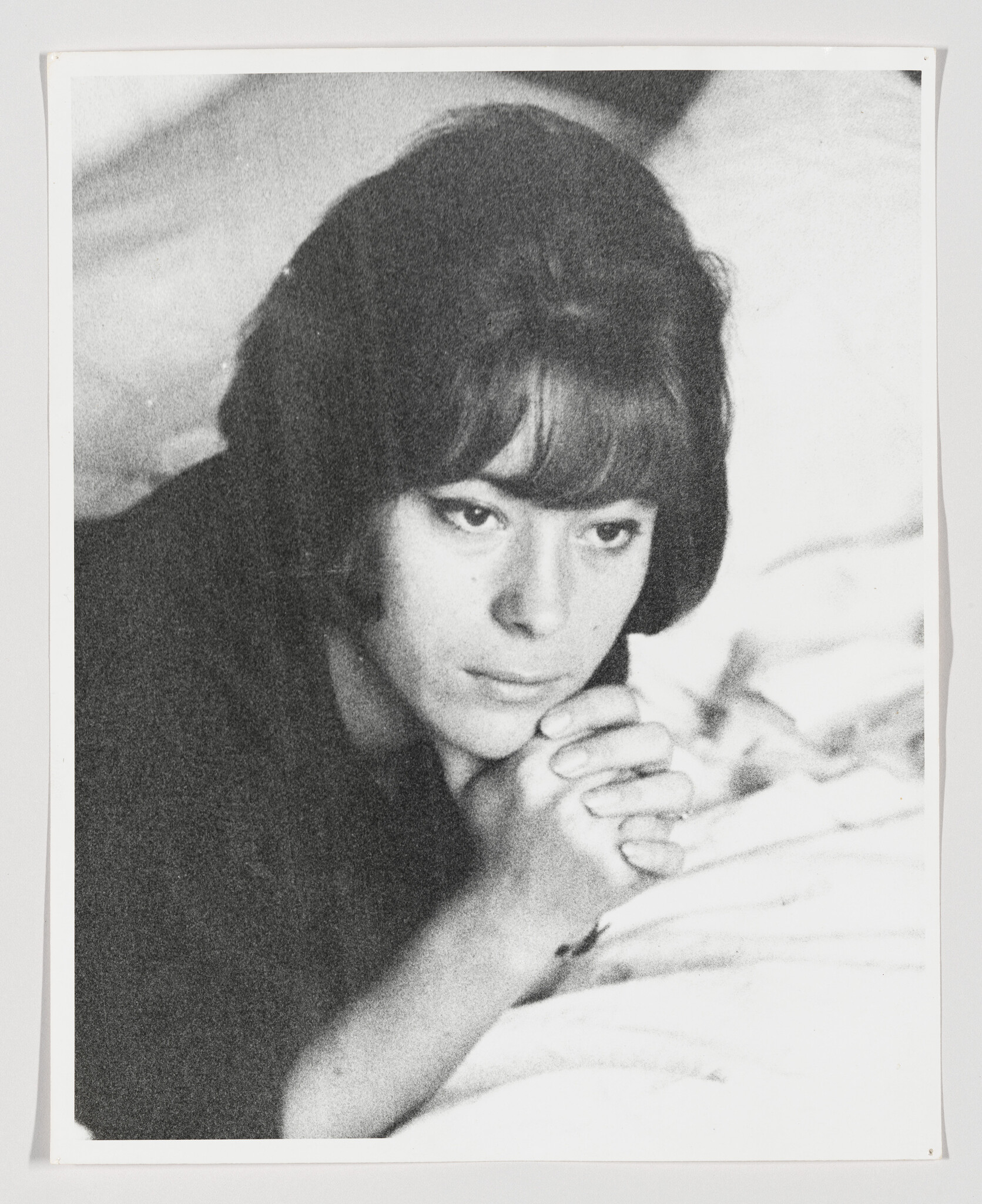 A young woman lies on a bed with hands clasped, looking thoughtful and pensive.