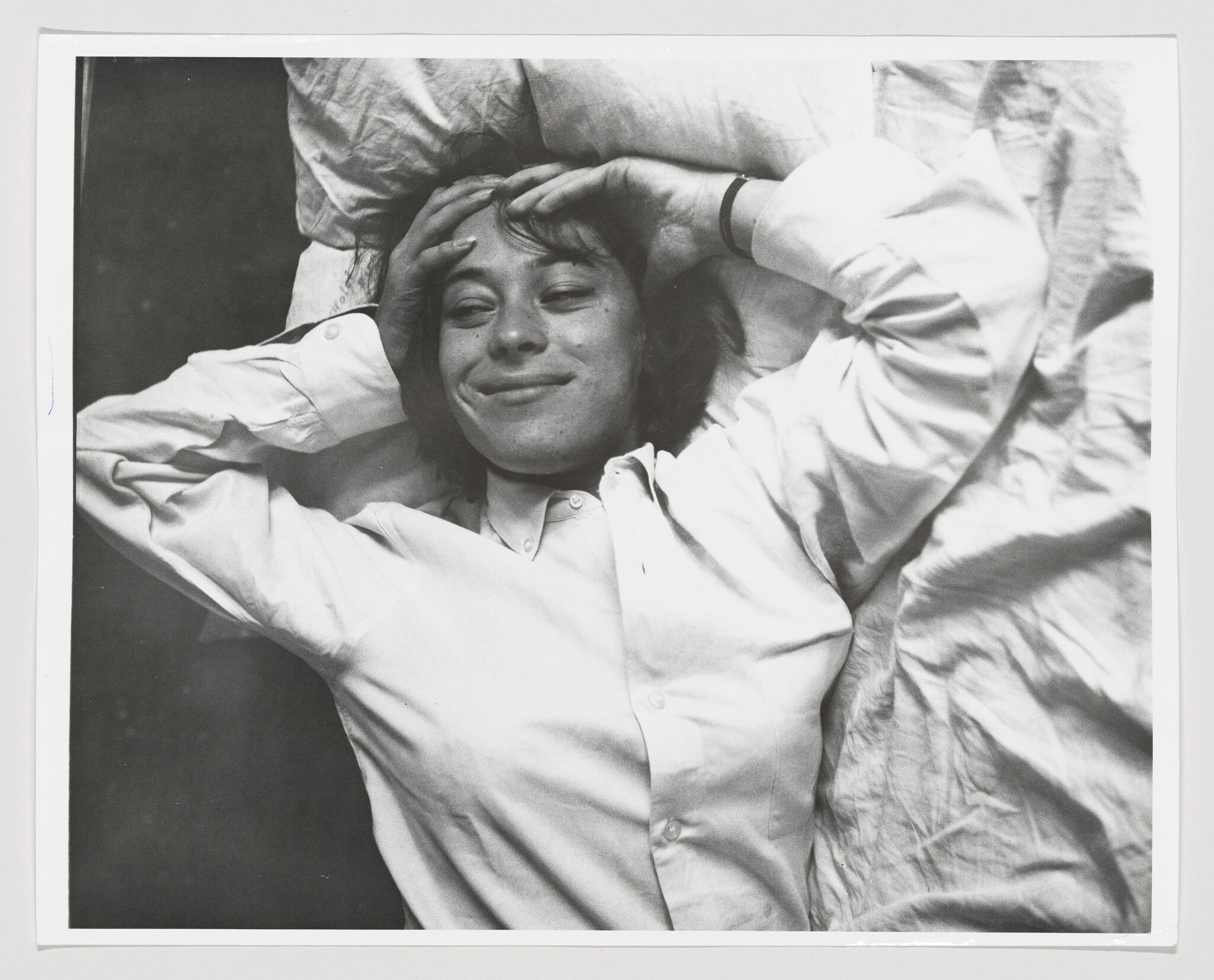 Person lying on a bed with hands behind their head and a relaxed smile.