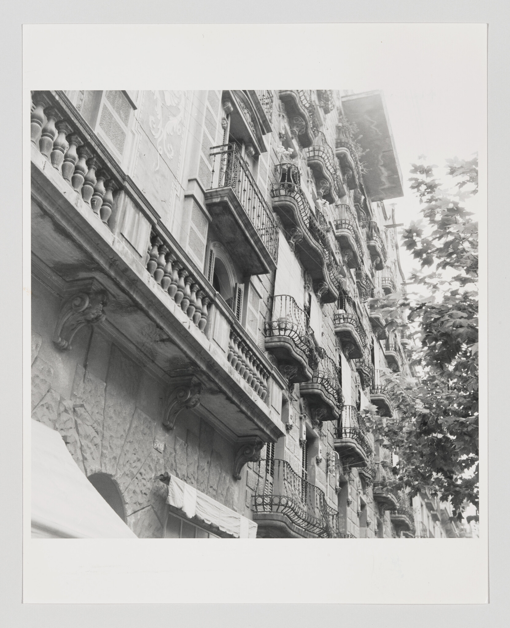 An ornate stone building façade with stacked wrought-iron balconies rising beside leafy trees.