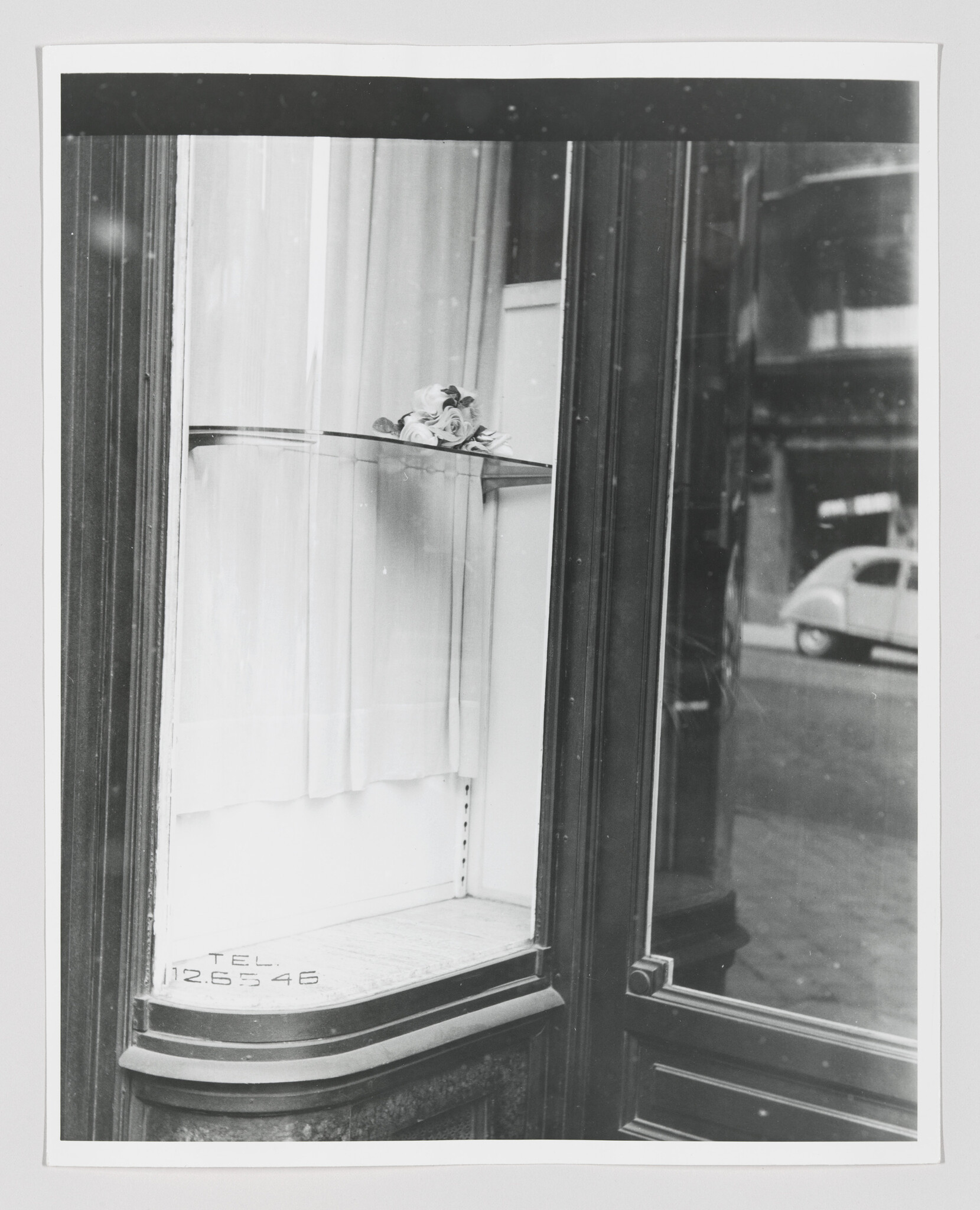 A small bouquet of roses rests on a glass shelf inside a shop window with street reflection.