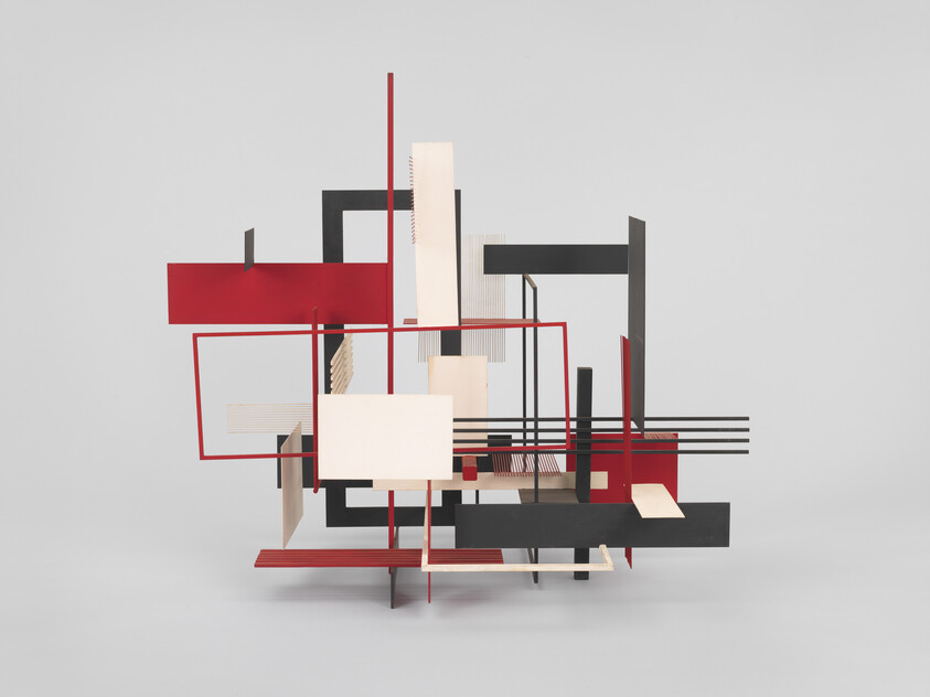 Abstract geometric sculpture of intersecting red, black, and beige rectangular planes and thin rods.