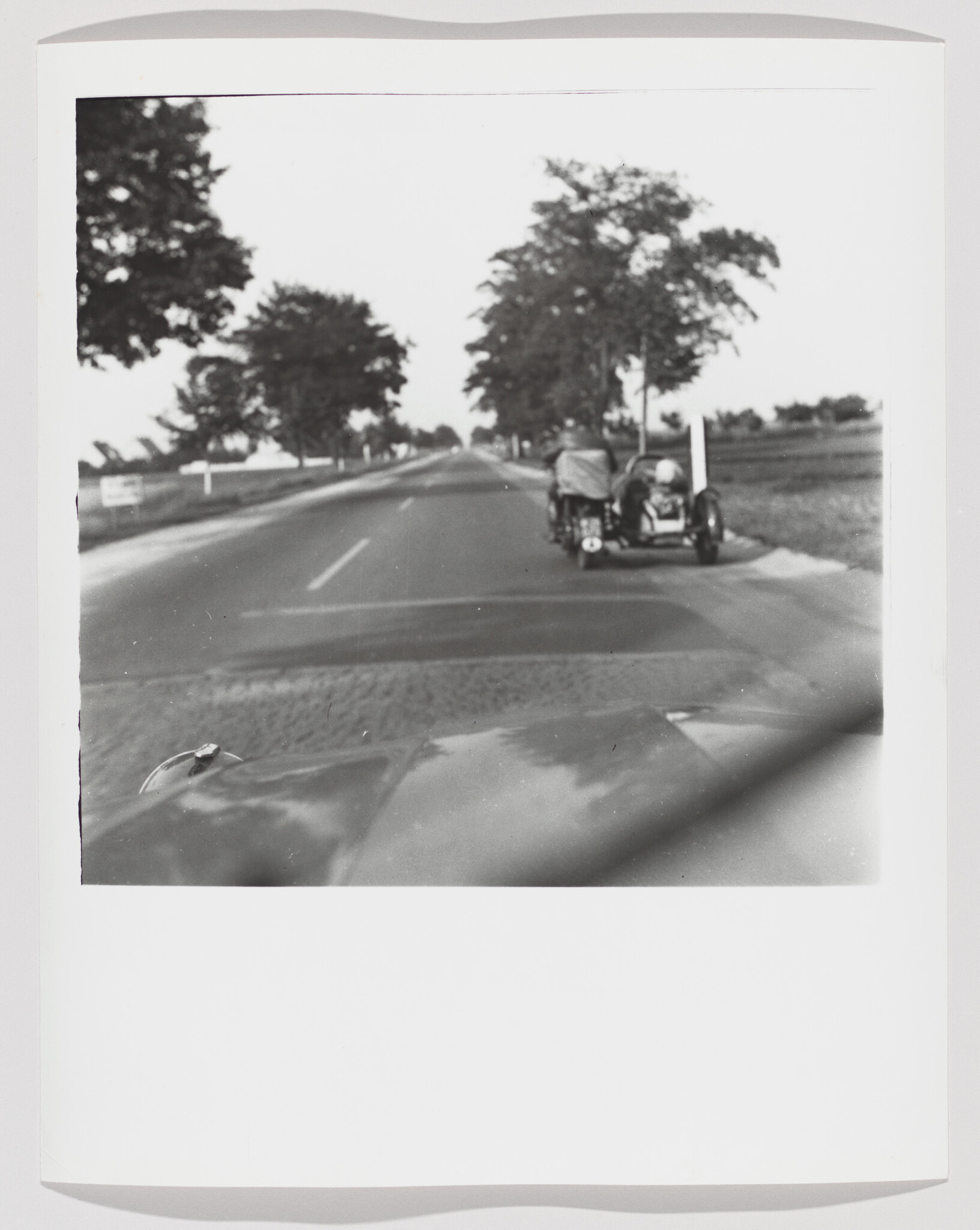 A motorcycle with a sidecar parked on the roadside while a car waits behind.
