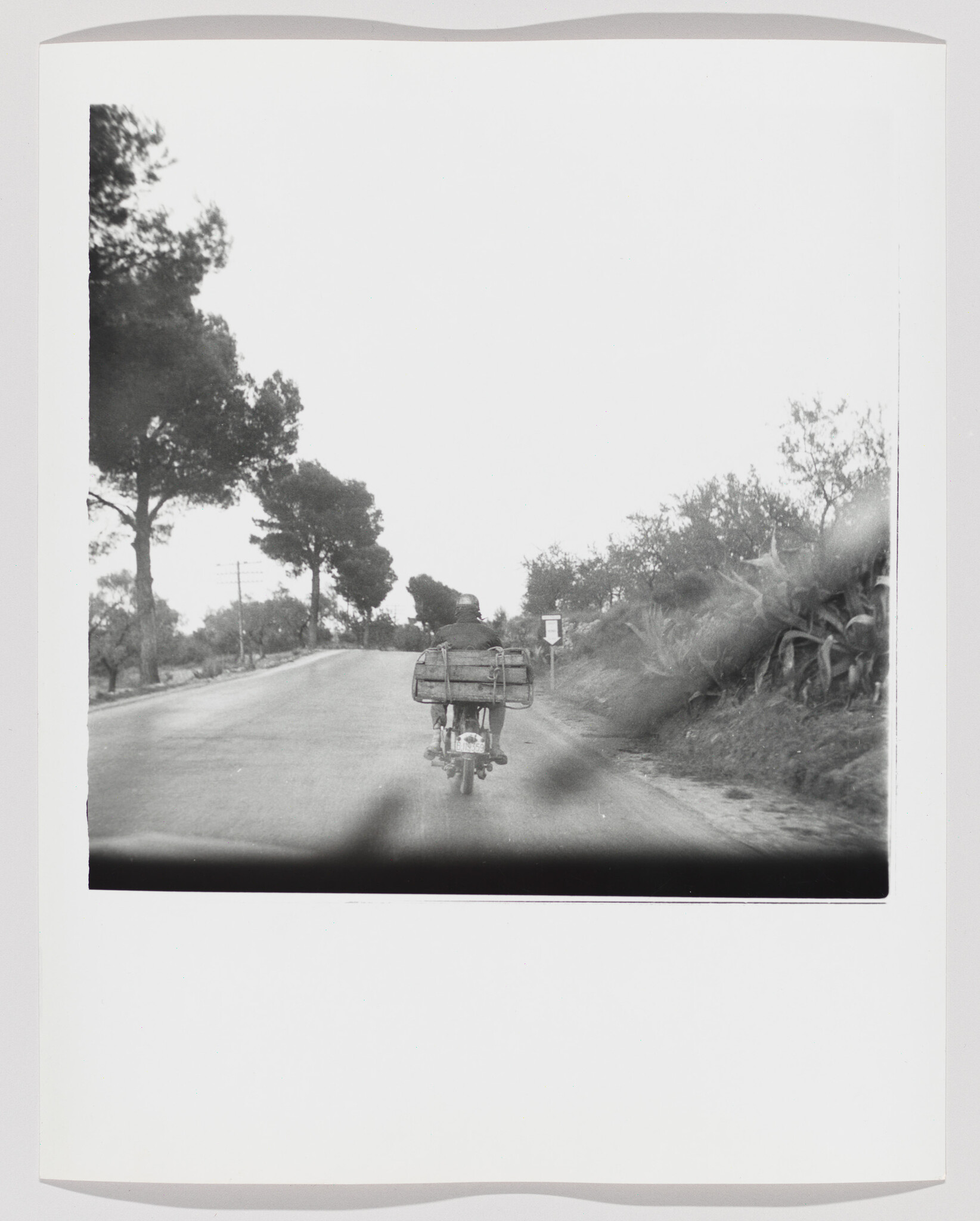 A rider on a motorcycle carries large packed bags while driving down a quiet rural road.