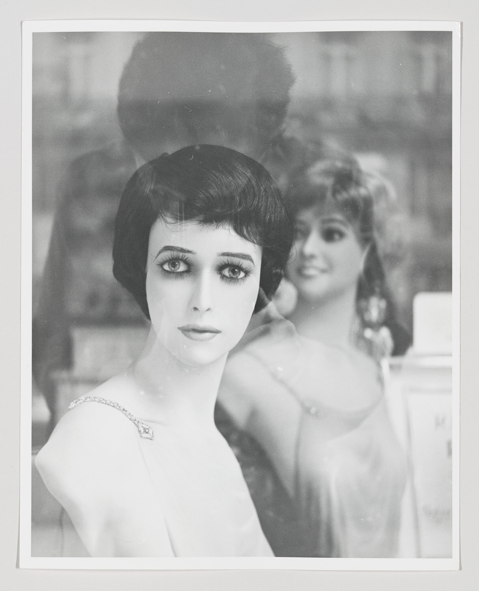 A lifelike mannequin with short dark hair faces the camera behind a shop window.