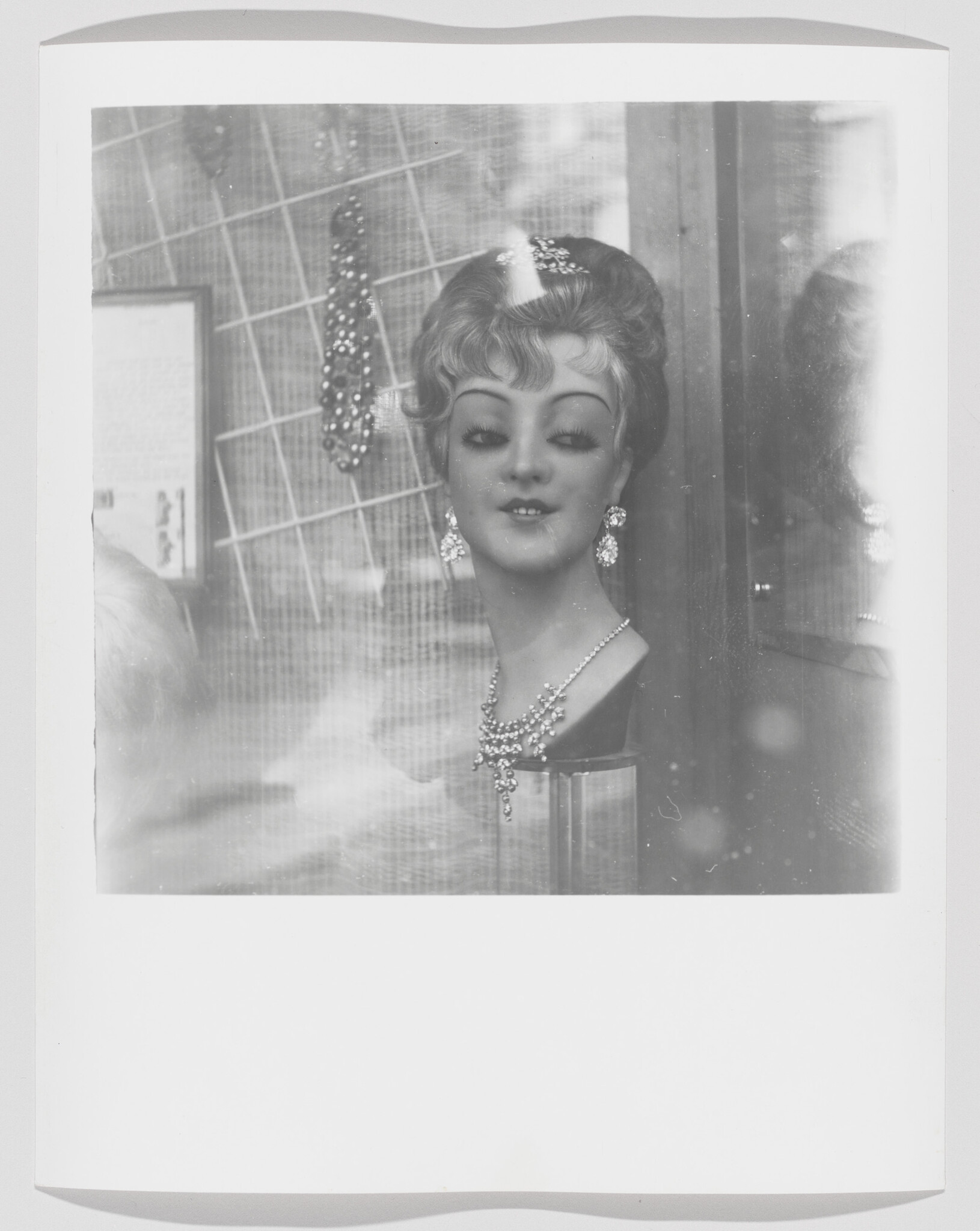 Mannequin head in a shop window modeling a necklace and dangling earrings.