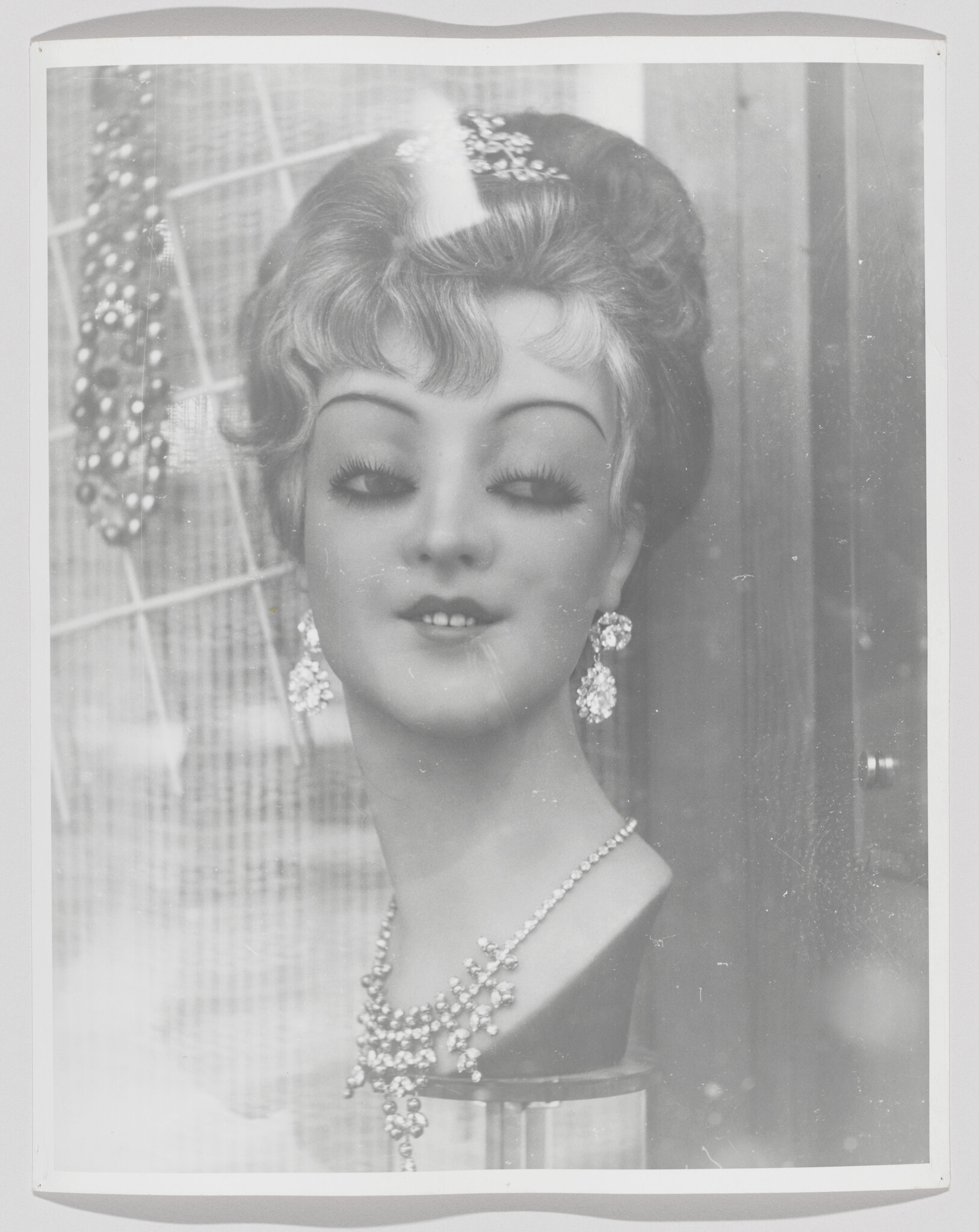 Mannequin head with styled hair wearing rhinestone earrings and a jeweled necklace in a display.