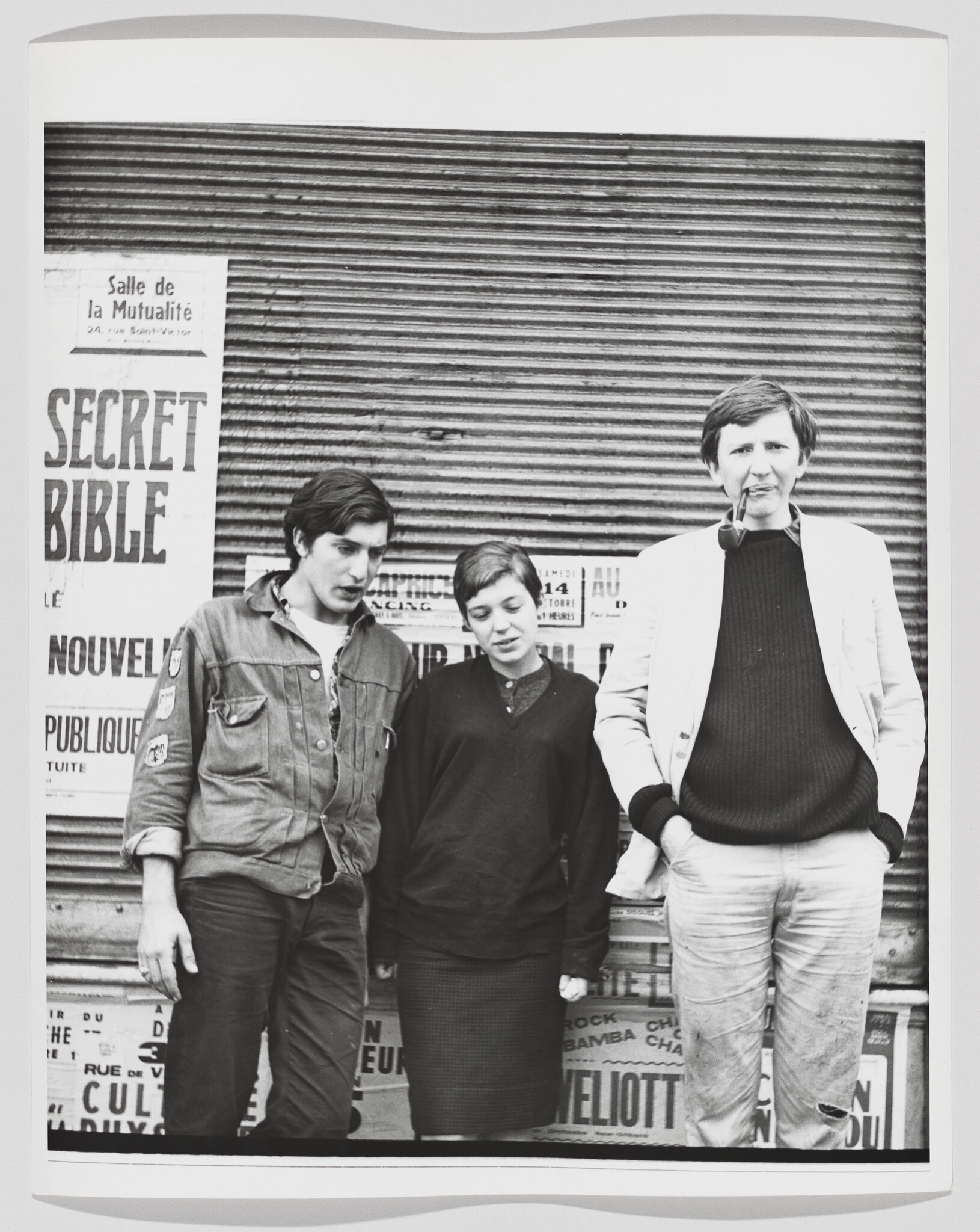Three young adults stand against a shuttered storefront with a poster reading "Secret Bible."