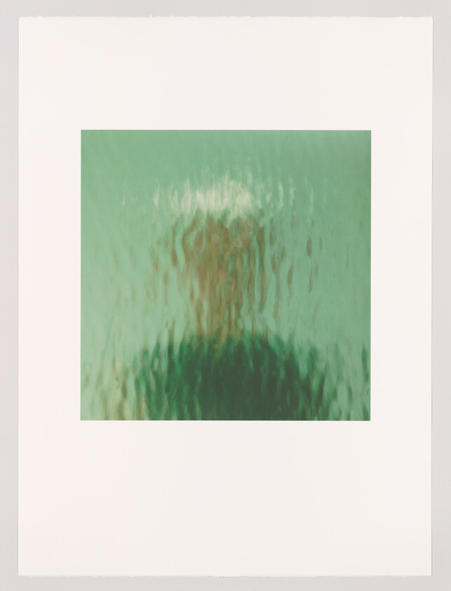 Blurry silhouette of a person seen through rippled green glass, creating a distorted outline.