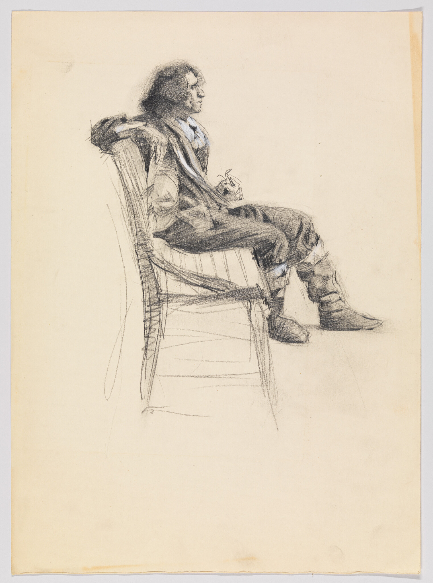 Man in loose clothing sits sideways on a chair, leaning back with hands clasped.