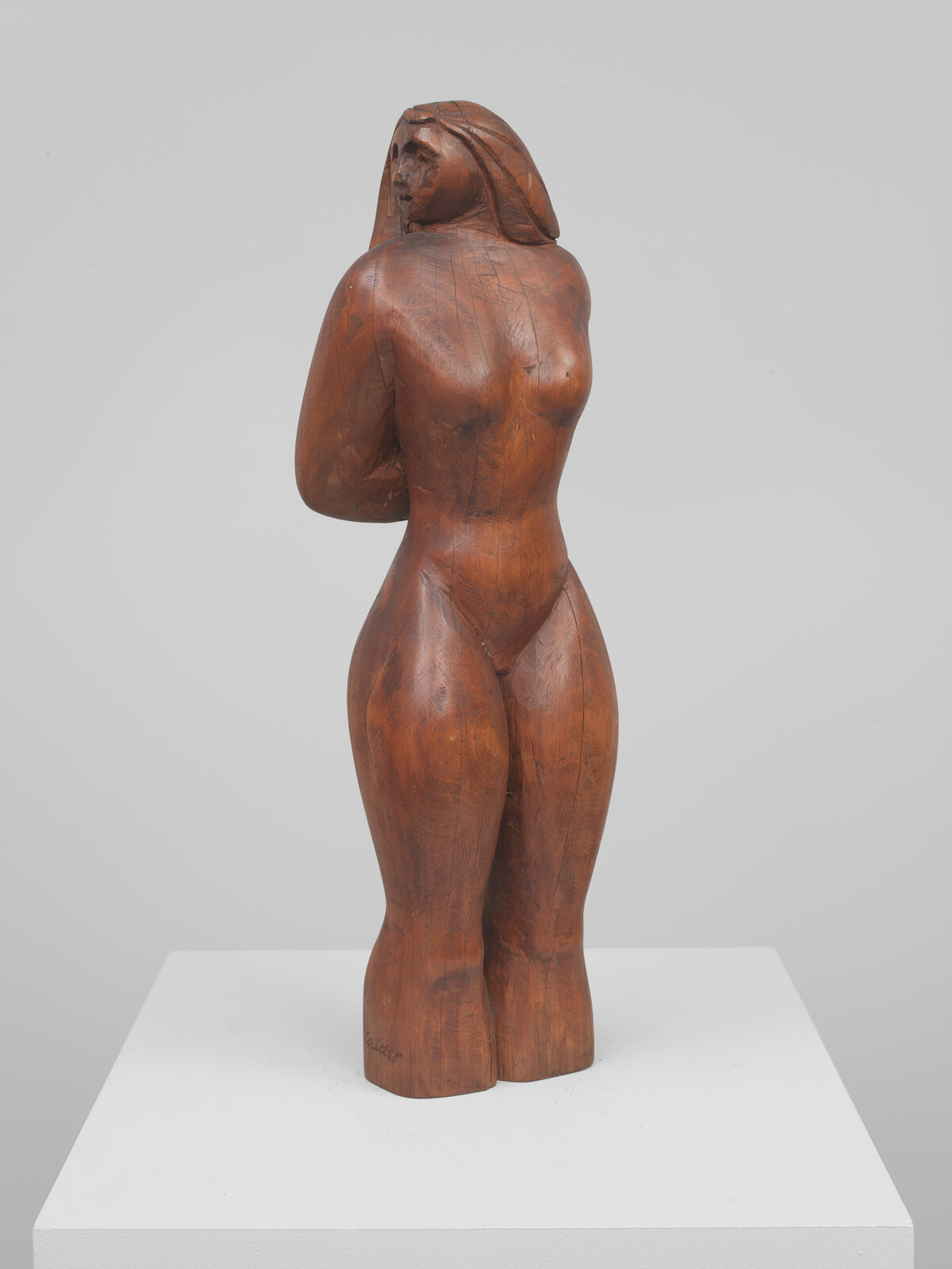 Carved wooden sculpture of a standing nude woman with arms behind her back looking over her shoulder.