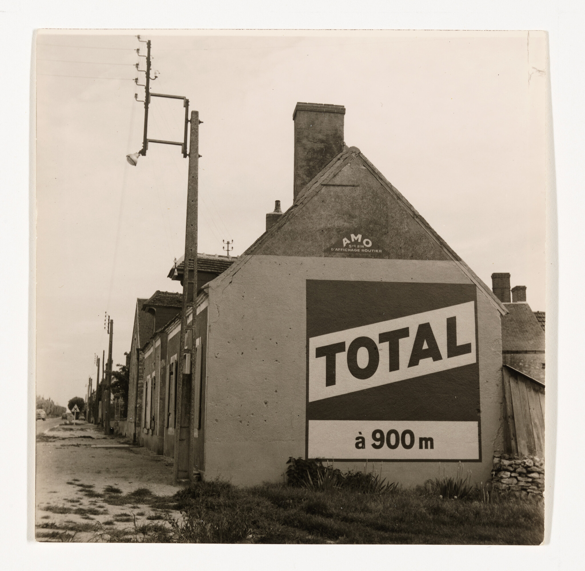 Large TOTAL roadside sign painted on a village house wall indicating a service station 900 meters away.