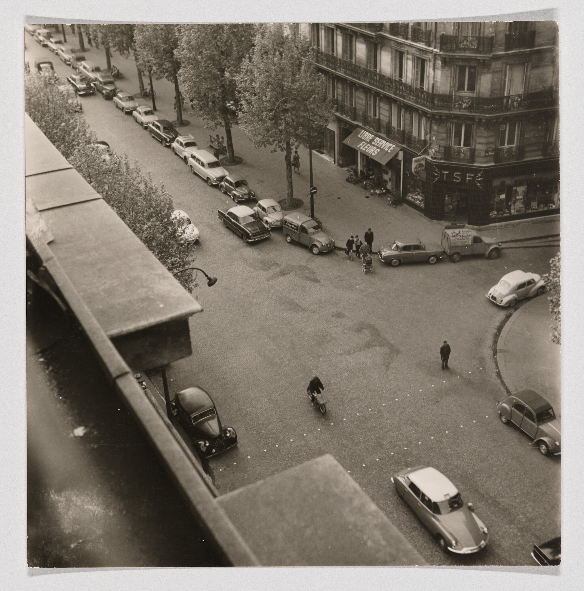 Aerial view of a city intersection with parked vintage cars, a cyclist, and pedestrians.