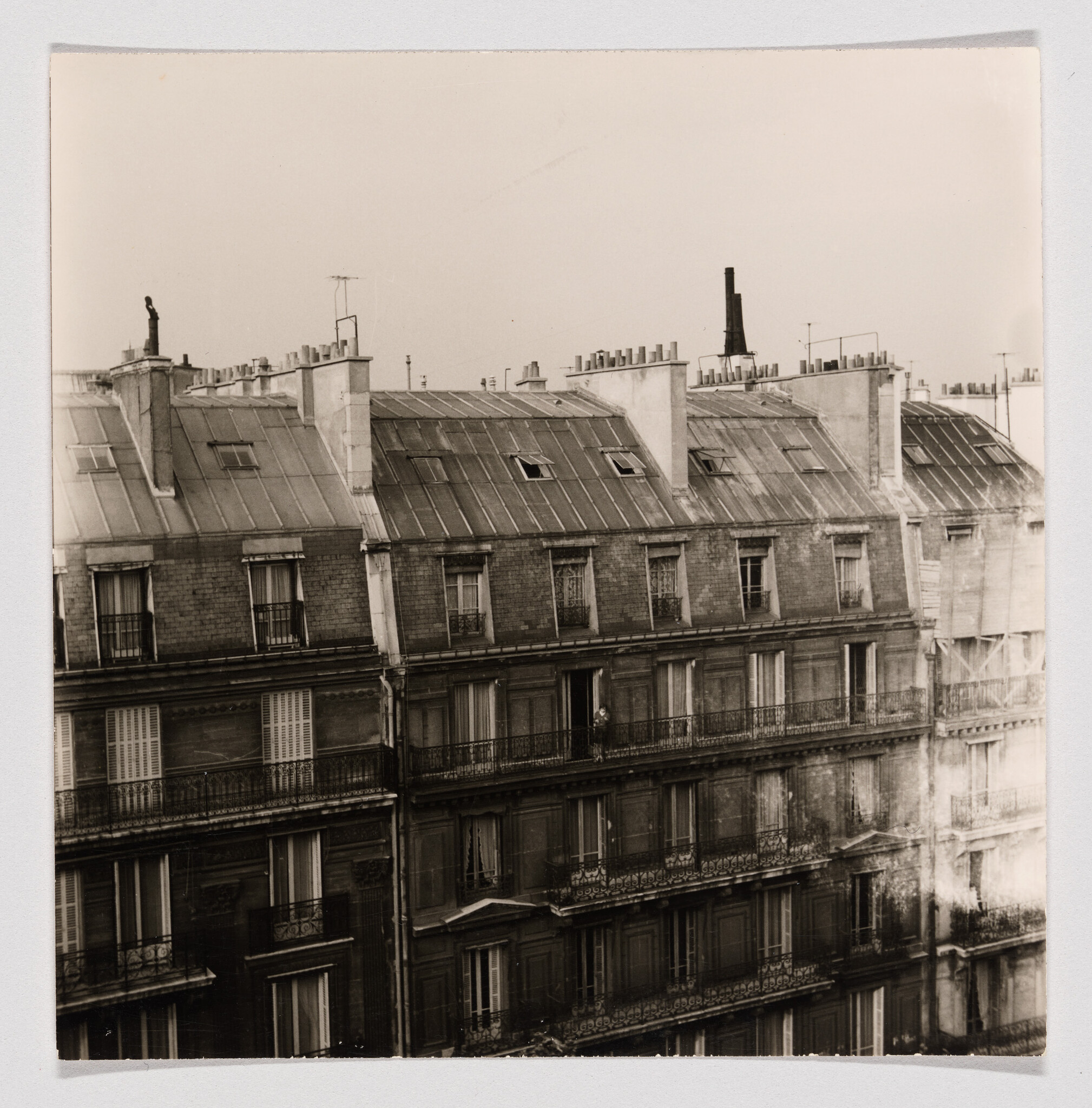 Old multi-story Parisian apartment building with mansard roof and a person standing on a central balcony.