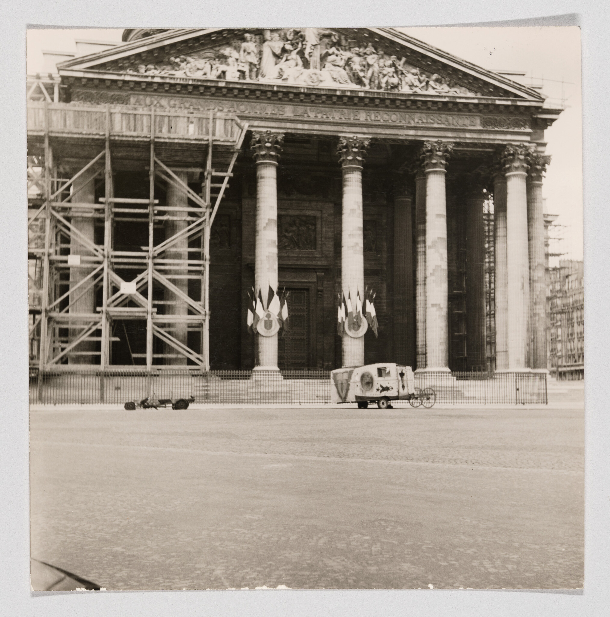 Large columned building under repair with scaffolding and a small decorated vehicle parked in front.