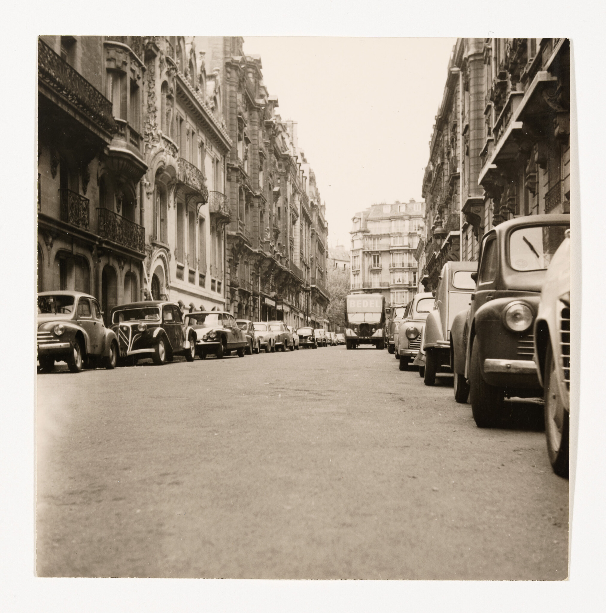 A row of vintage cars parked along a narrow street between ornate apartment buildings.