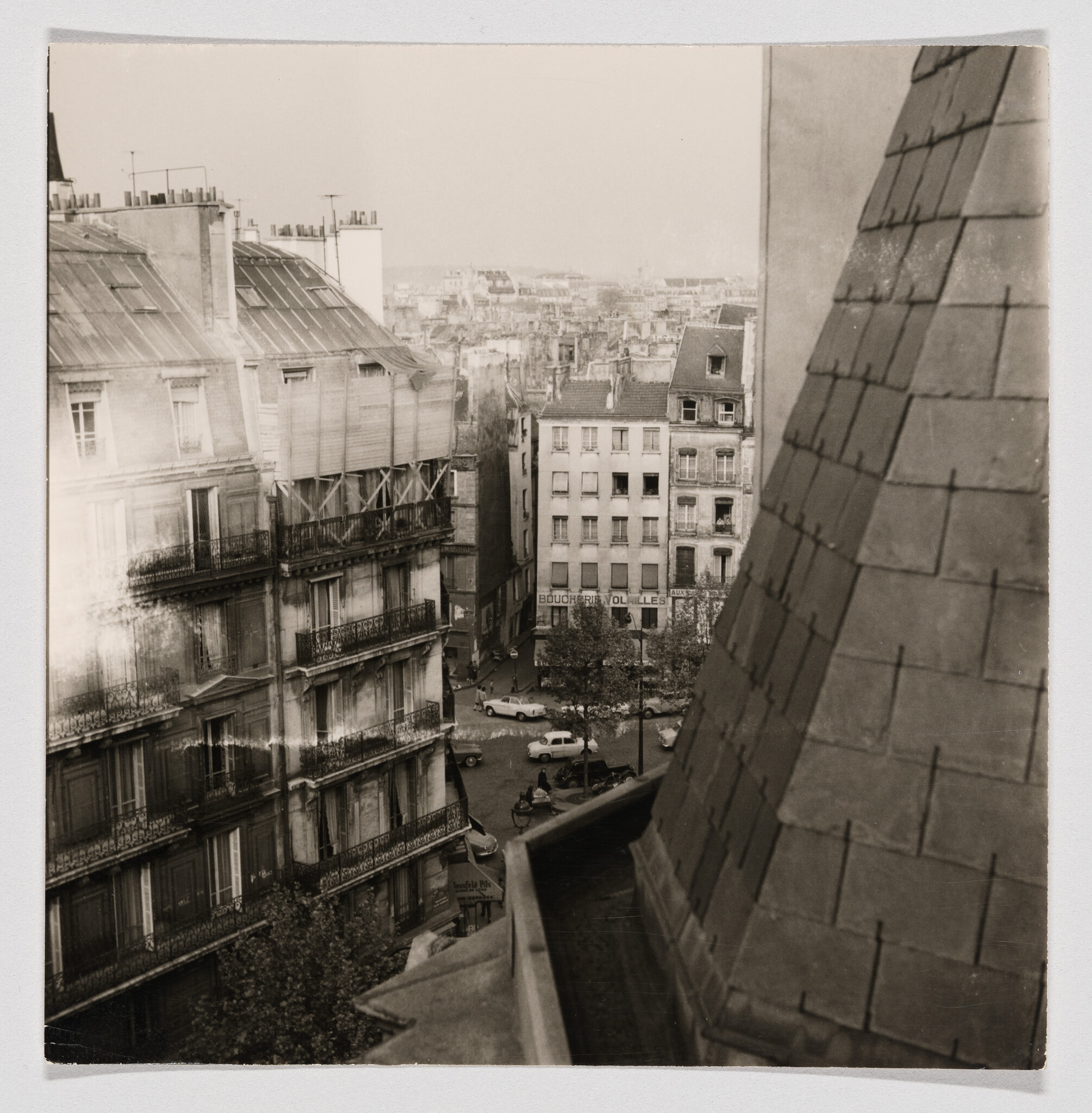Rooftop view over a Paris street with old apartment buildings and parked cars.
