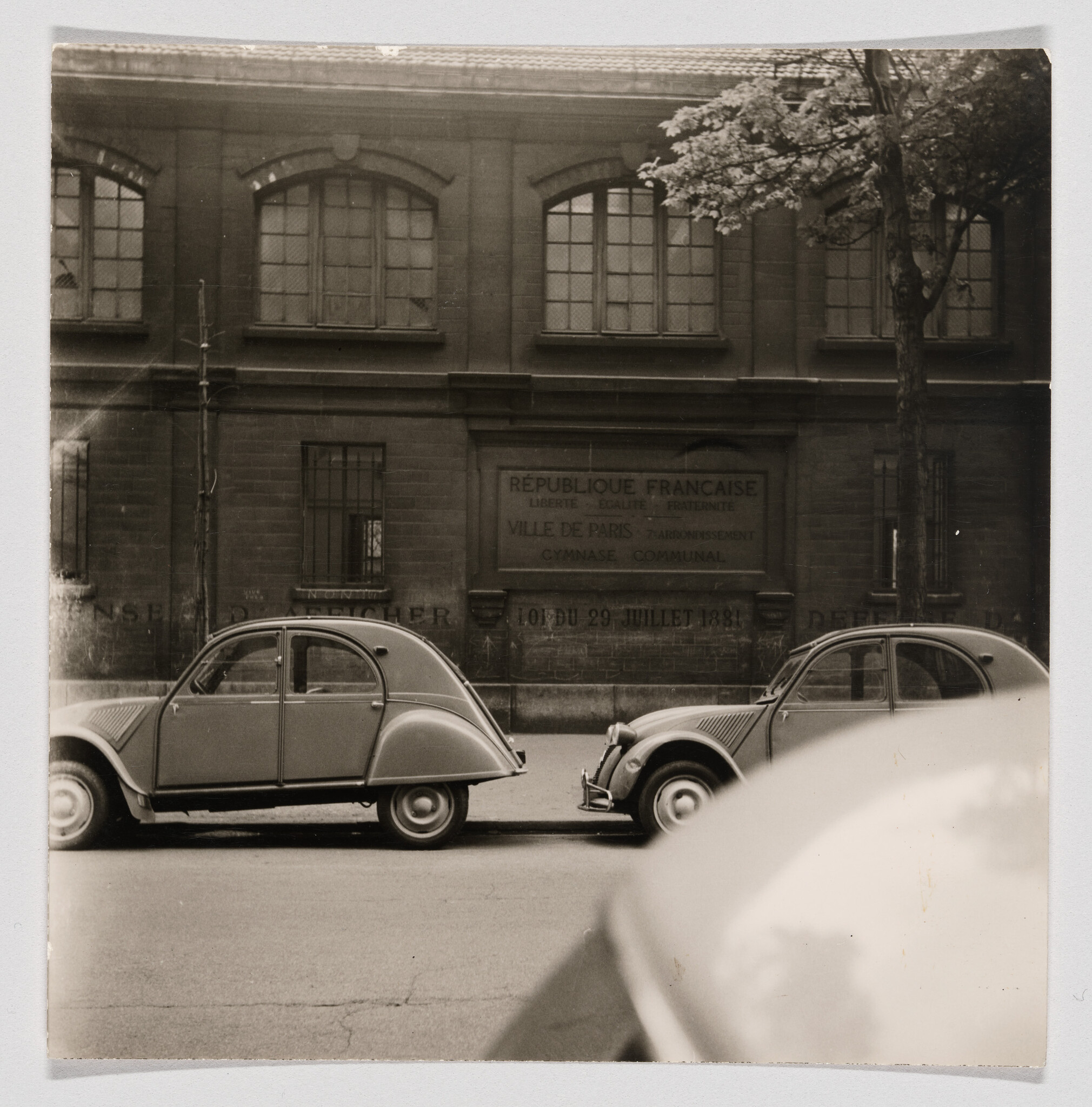 Two vintage Citroën 2CV cars parked on a street in front of a building reading République Française.